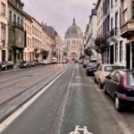 Stadtstraße mit Fahrradspur, parkenden Autos und Blick auf die Église Sainte-Marie in Brüssel.