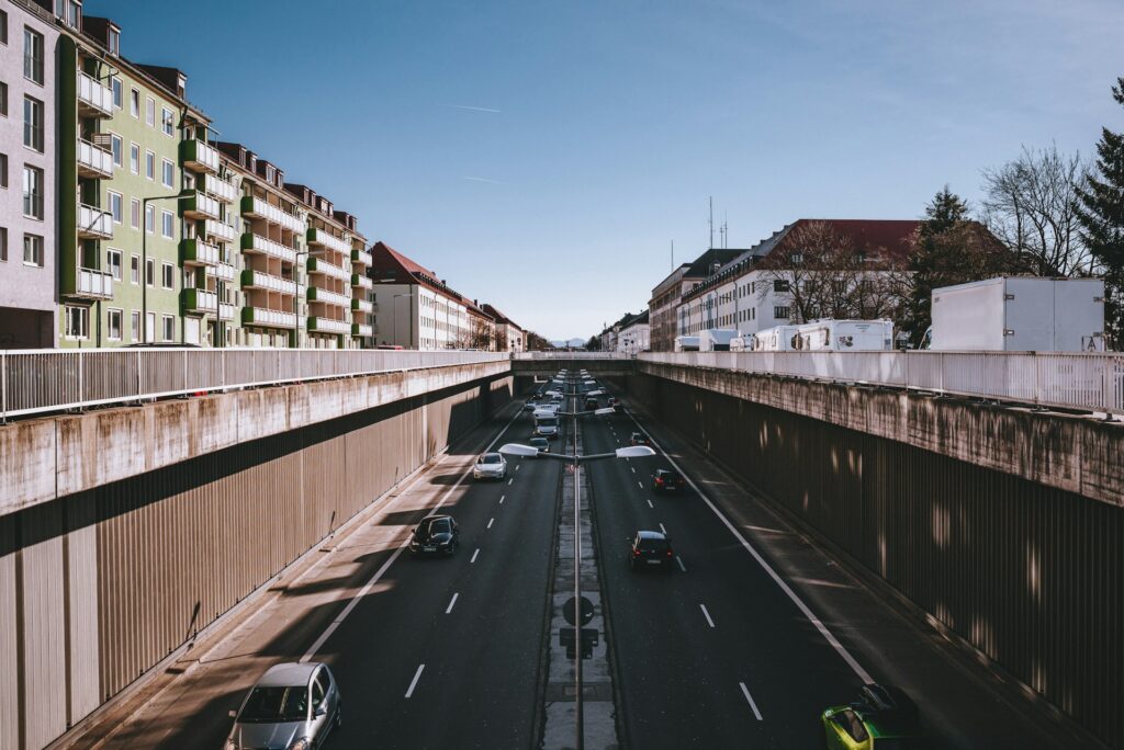 Autos auf der Straße zwischen braunen Betongebäuden unter blauem Himmel tagsüber in München.
