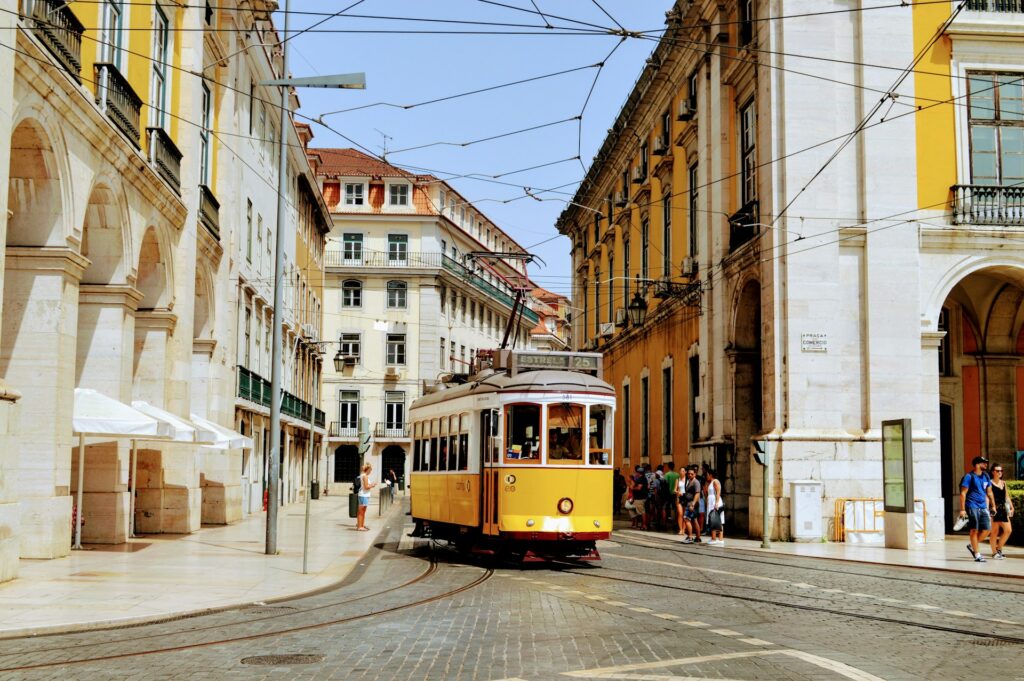 Eine gelb-weiße Straßenbahn ist tagsüber auf der Straße in Lissabon unterwegs.