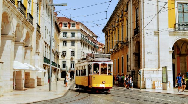 Eine gelb-weiße Straßenbahn ist tagsüber auf der Straße in Lissabon unterwegs.