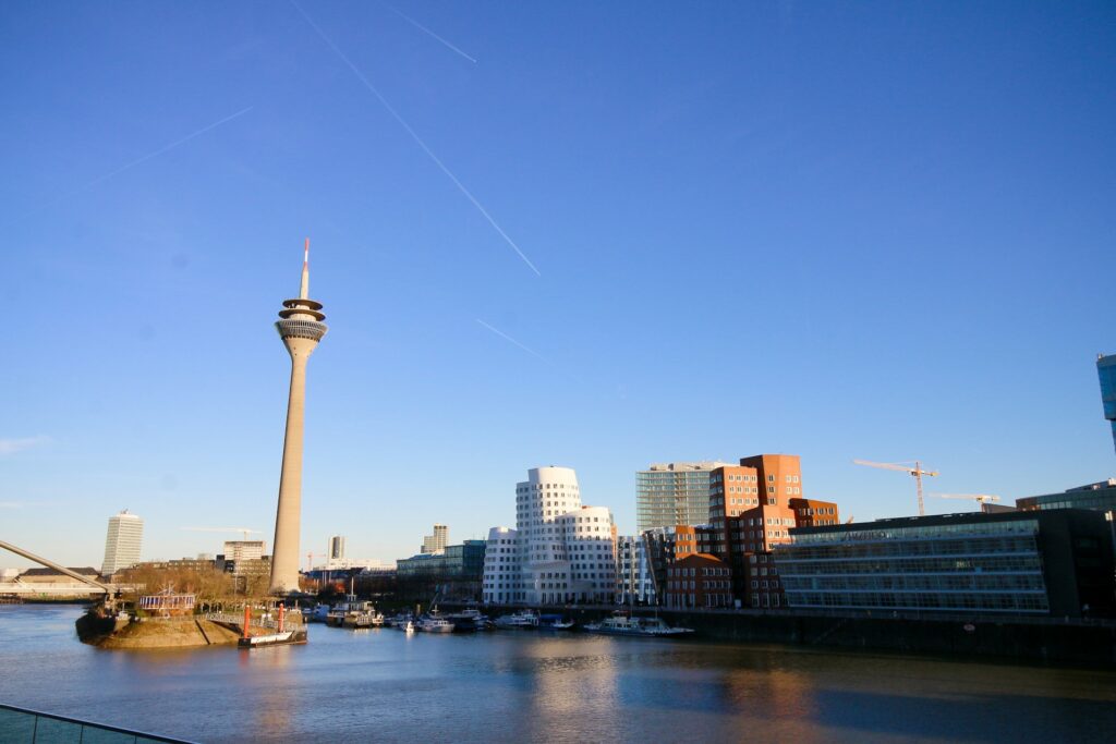 Blick auf einen Fluss in Düsseldorf mit einem Turm im Hintergrund und Spiegelungen auf der Wasseroberfläche.