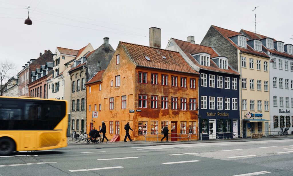 Ein gelber Bus fährt eine Straße entlang neben hohen Gebäuden in Kopenhagen.
