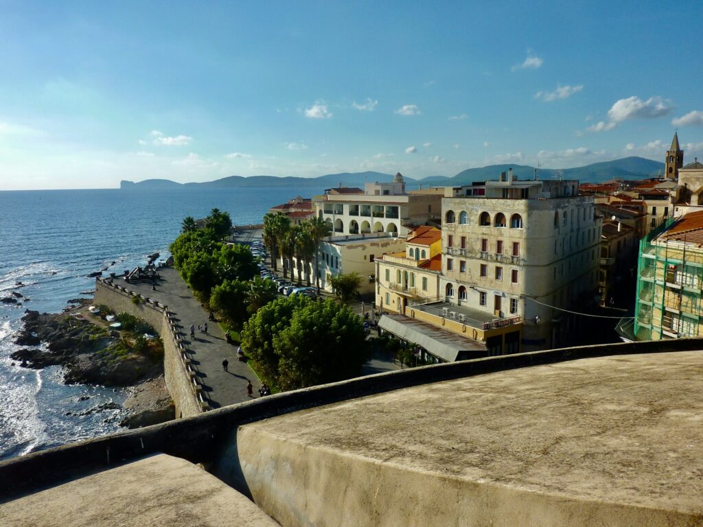 Küstenpromenade und Altstadt von Alghero mit Blick auf das Mittelmeer bei klarem Himmel auf Sardinien.