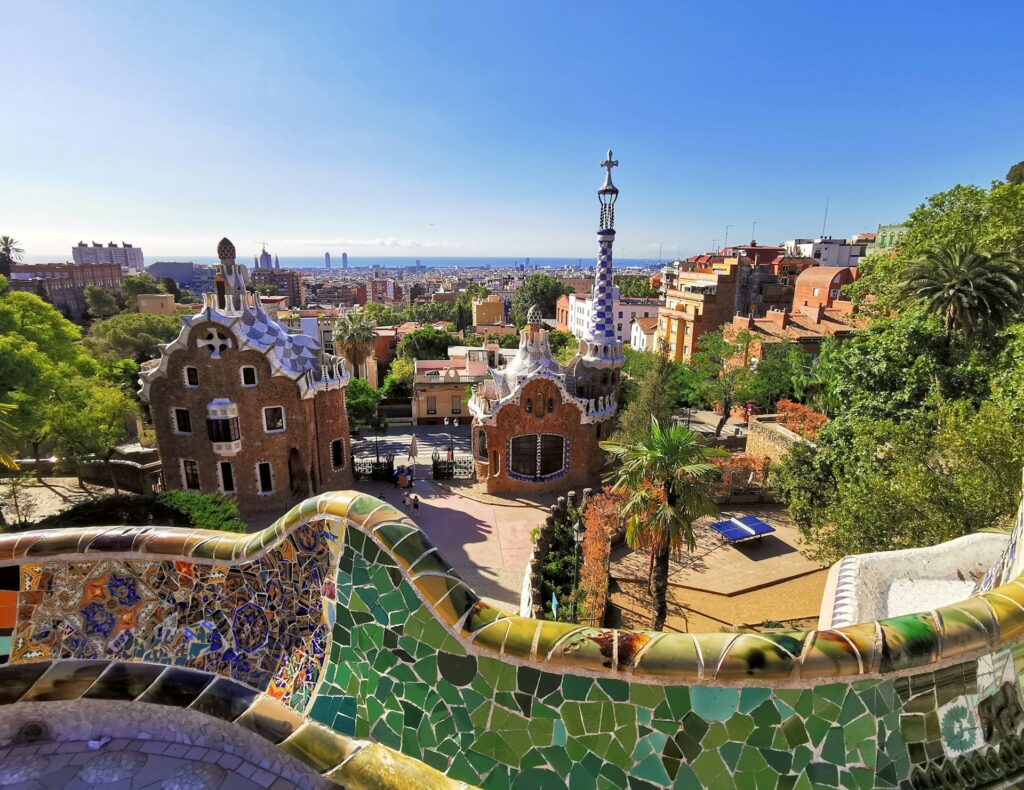 Bunte Mosaikbänke und fantasievolle Gebäude im Park Güell mit Blick auf Barcelona und das Meer.