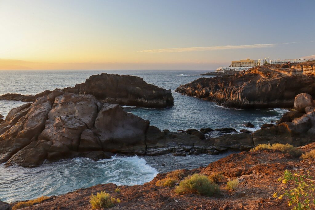 Küstenlandschaft mit vulkanischen Felsen und Hotels bei Sonnenuntergang auf Teneriffa, Kanarische Inseln.