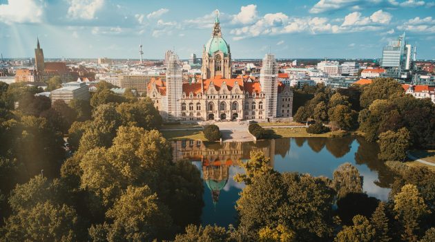 Luftaufnahme des Neuen Rathauses in Hannover mit grüner Kuppel, umgeben von Bäumen und dem Maschteich.