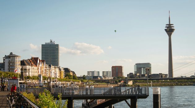 Skyline von Düsseldorf mit dem Rheinturm und der Rheinpromenade an einem sonnigen Tag.