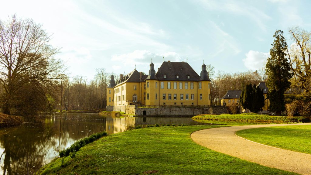 Wasserschloss Dyck in Jüchen mit Burggraben, Parkanlage und geschwungenem Weg im Vordergrund.