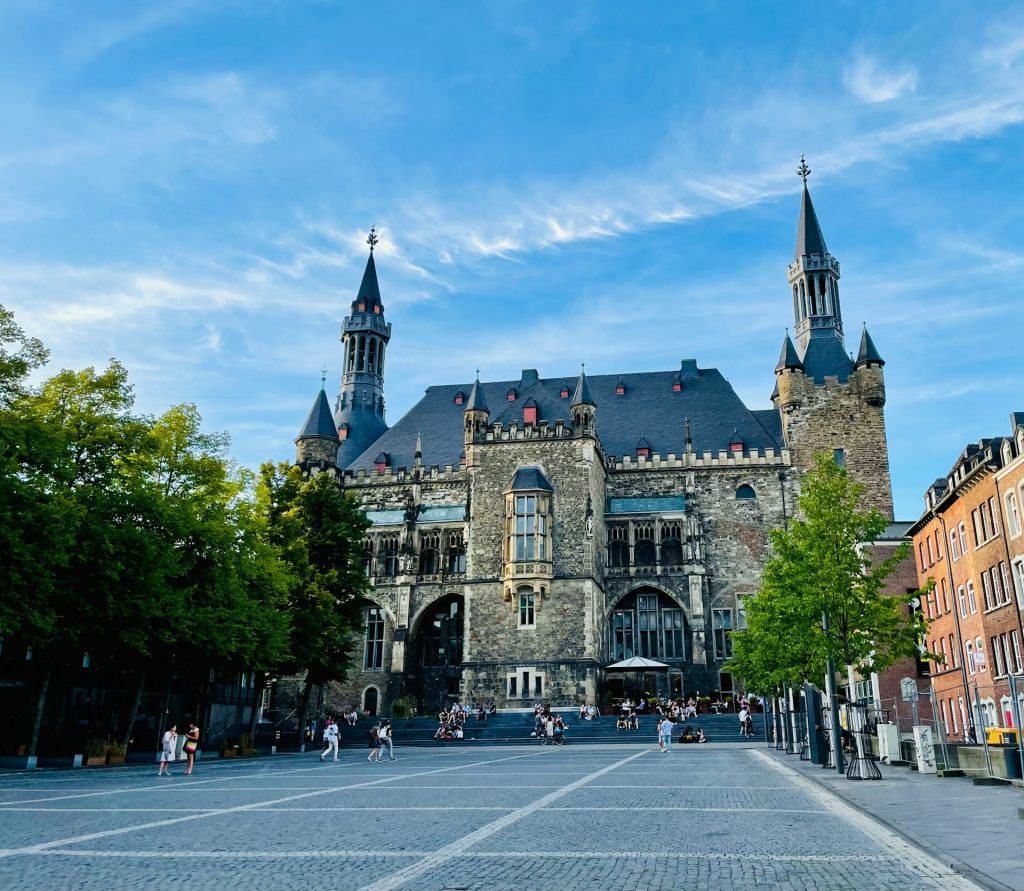 Aachener Rathaus mit Marktplatz im Vordergrund und blauem Himmel im Sommer.