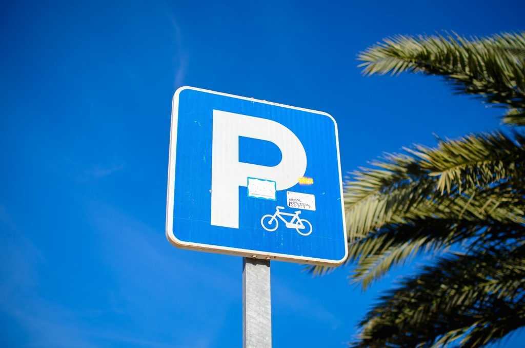 Blaues Parkschild mit Fahrradsymbol vor blauem Himmel und Palmen.