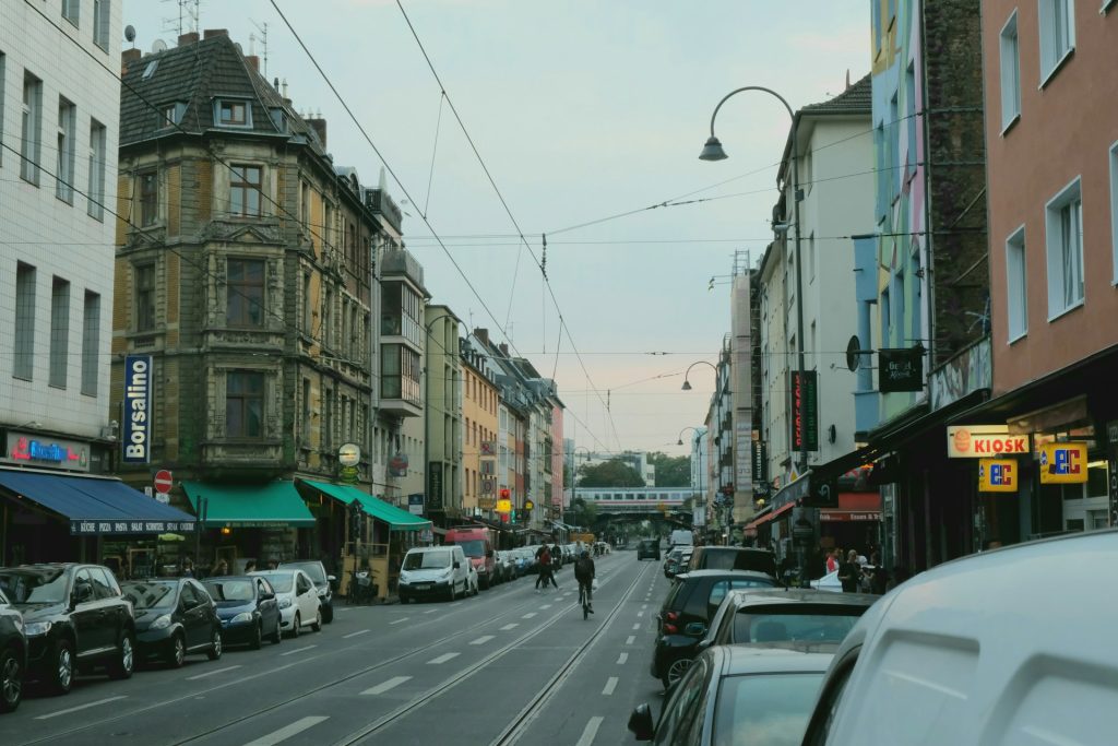 Belebte Kölner Innenstadt mit Autos, Straßenbahn und Geschäften entlang einer mehrspurigen Straße.