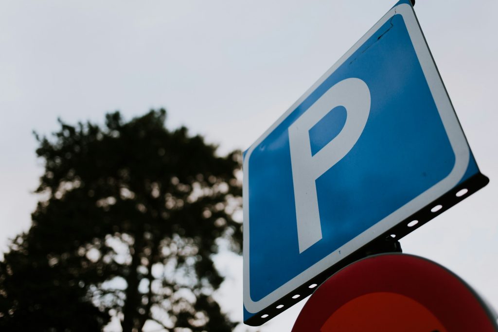 Blaues Parkschild vor einem Baum und bewölktem Himmel.