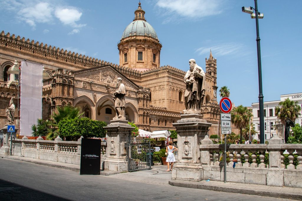 Kathedrale von Palermo mit großer Kuppel, Statuen und Palmen unter blauem Himmel.