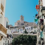 Enge Gasse in der Ibiza-Altstadt mit weißen Häusern und der Kathedrale von Dalt Vila im Hintergrund.