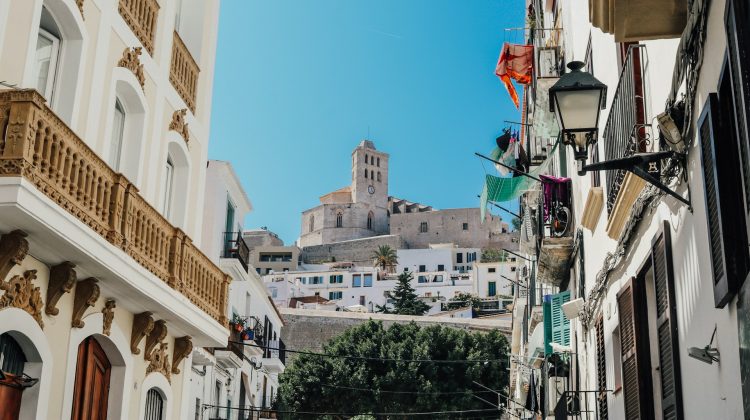 Enge Gasse in der Ibiza-Altstadt mit weißen Häusern und der Kathedrale von Dalt Vila im Hintergrund.