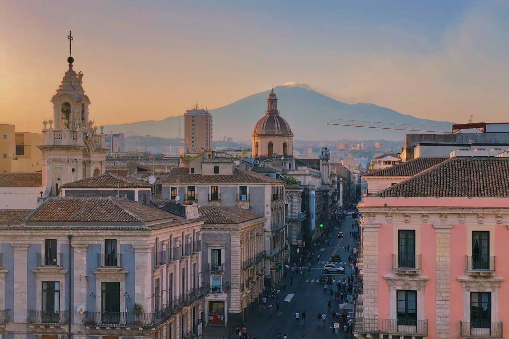 Blick über die Altstadt von Catania mit barocken Gebäuden, einer Kirchenkuppel und dem Ätna im Hintergrund.