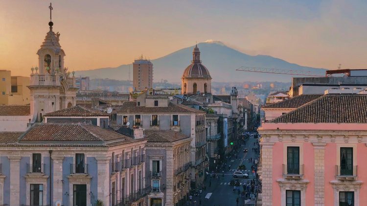 Blick über die Altstadt von Catania mit barocken Gebäuden, einer Kirchenkuppel und dem Ätna im Hintergrund.