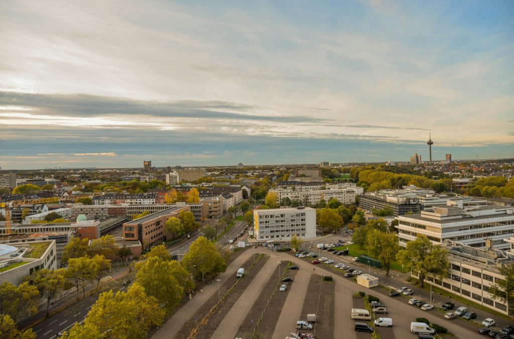 Luftaufnahme von Köln mit Parkplätzen, Herbstbäumen und dem Colonius-Fernsehturm im Hintergrund.