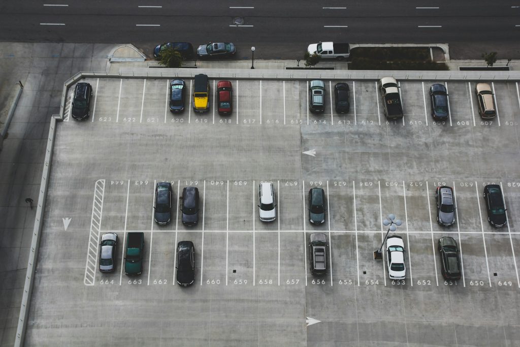 Luftaufnahme eines teils besetzten Parkplatzes mit nummerierten Stellplätzen und vereinzelten Fahrzeugen.
