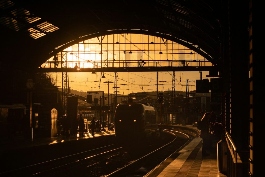 Zug fährt bei Sonnenuntergang in den Aachener Hauptbahnhof ein mit Reisenden auf dem Bahnsteig.