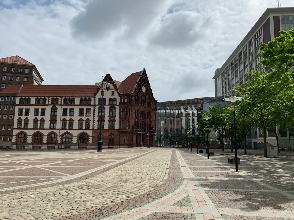 Leerer Hansaplatz in Dortmund mit historischem Rathaus und modernem Glasgebäude bei bewölktem Himmel.