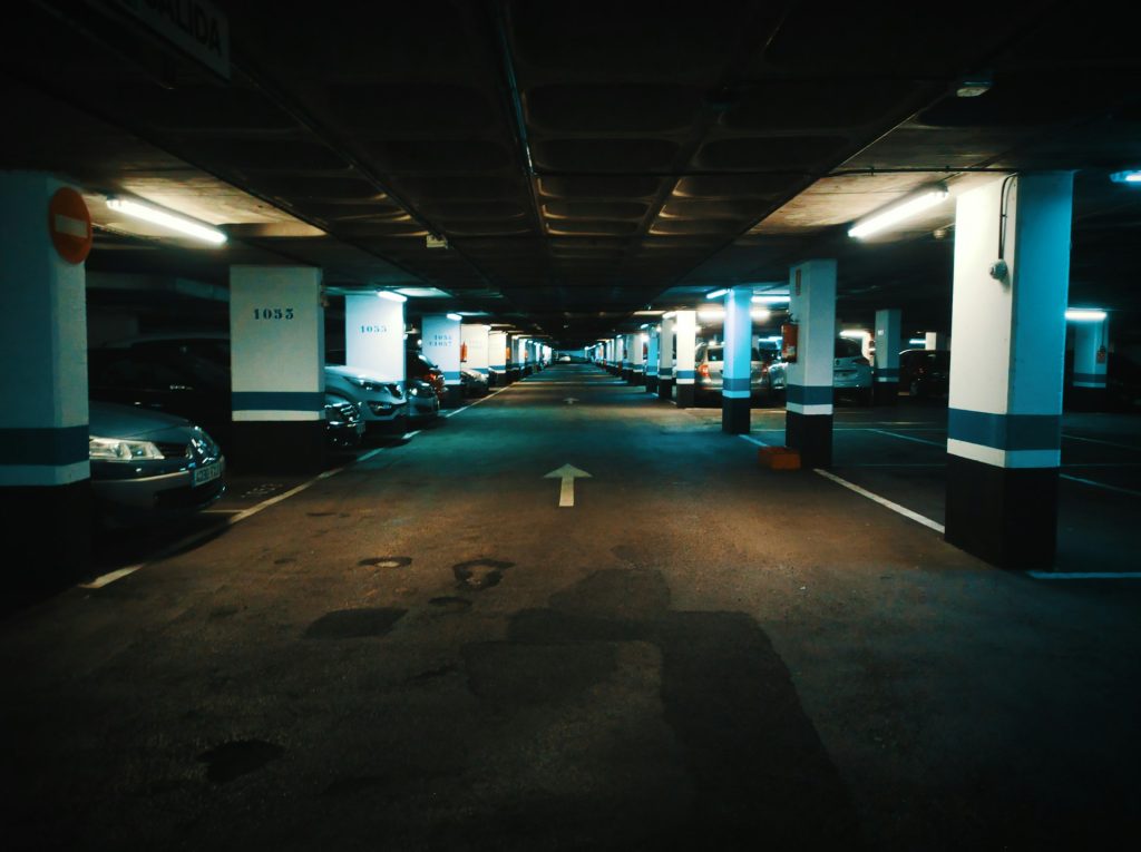 Beleuchtete Tiefgarage mit geparkten Autos und Richtungspfeil auf dem Boden.