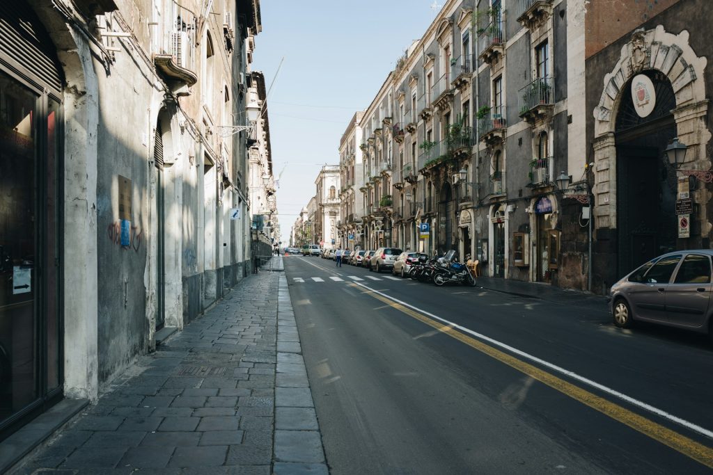 Ruhige Straße in Catanias Altstadt mit geparkten Autos und barocken Gebäuden bei Tageslicht.