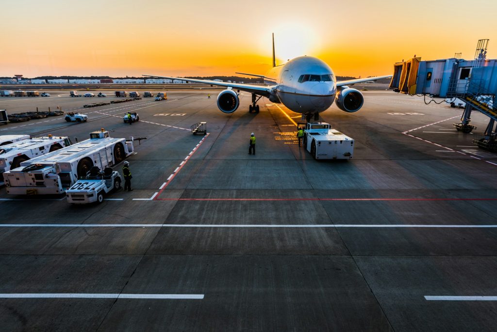 Passagierflugzeug auf dem Vorfeld bei Sonnenuntergang, umgeben von Bodenfahrzeugen und Personal.