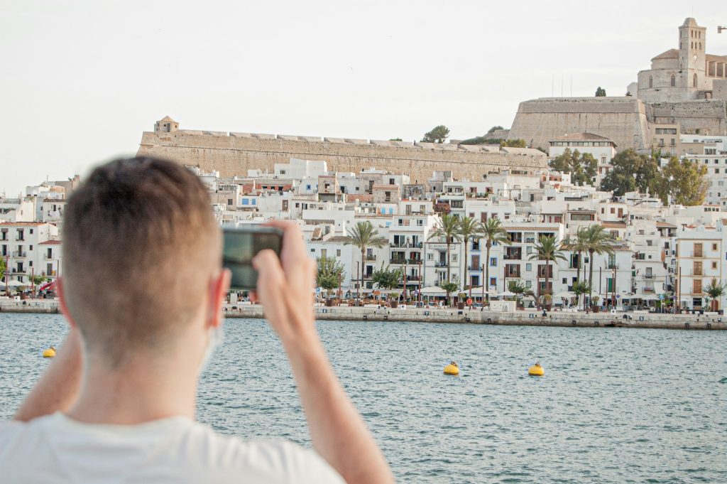 Mann fotografiert die weiße Hafenfront von Ibiza-Stadt mit Dalt Vila im Hintergrund.