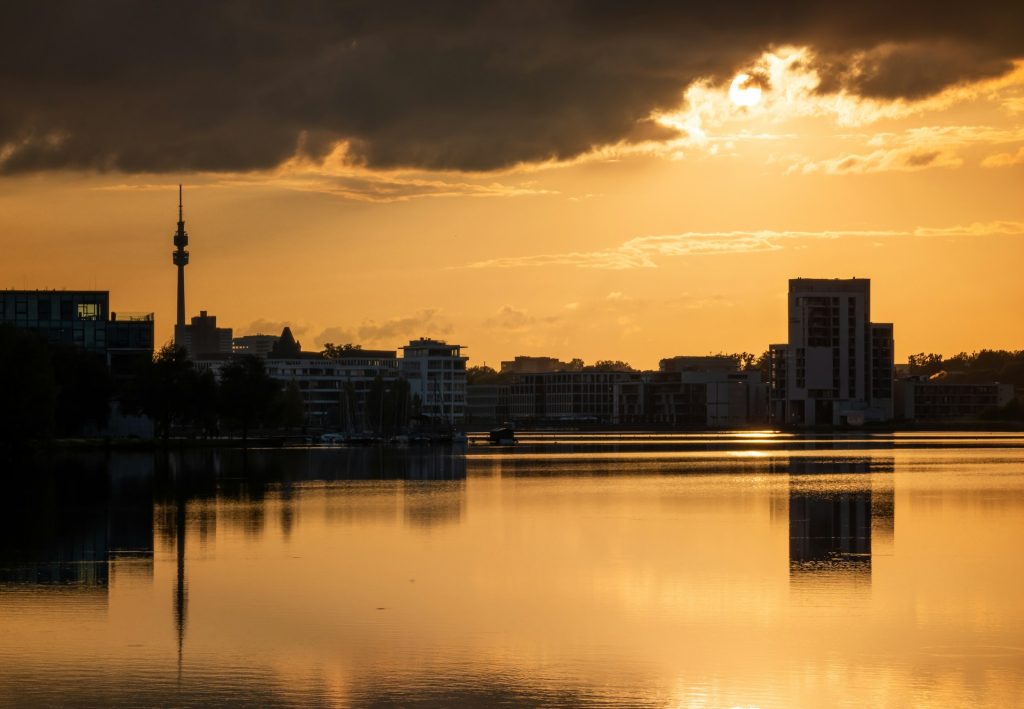 Stadtsilhouette Dortmunds mit Florianturm bei goldenem Sonnenuntergang, gespiegelt in einem ruhigen See.
