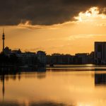 Stadtsilhouette Dortmunds mit Florianturm bei goldenem Sonnenuntergang, gespiegelt in einem ruhigen See.