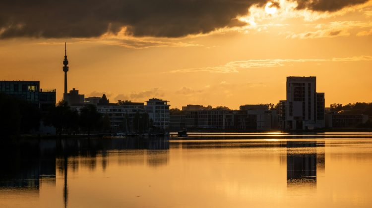Stadtsilhouette Dortmunds mit Florianturm bei goldenem Sonnenuntergang, gespiegelt in einem ruhigen See.