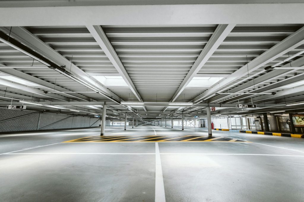 Leeres, modernes Parkhaus mit gelben Markierungen, Stahlträgern und Aufzugsbeschilderung.