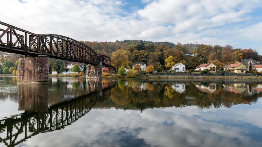 Historische Eisenbahnbrücke über die Weser in Hameln mit buntem Herbstlaub und Häusern im Hintergrund.