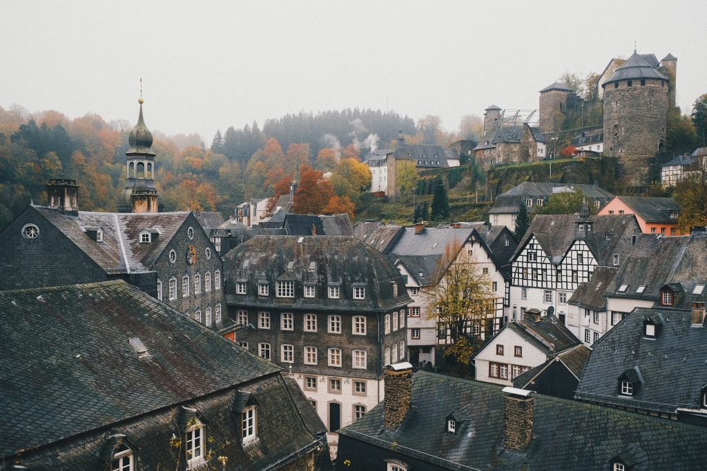 Herbstliche Dächer der Altstadt von Monschau mit Fachwerkhäusern, Kirchturm und Burg im Hintergrund.