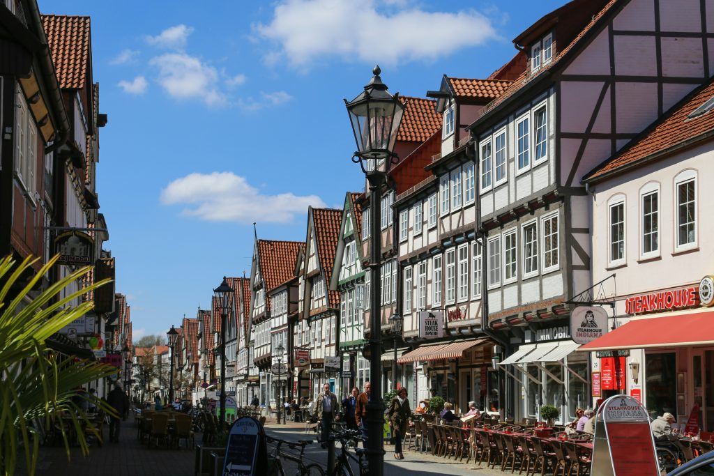 Belebte Fußgängerzone in Celle mit historischen Fachwerkhäusern, Cafés und einer alten Straßenlaterne.