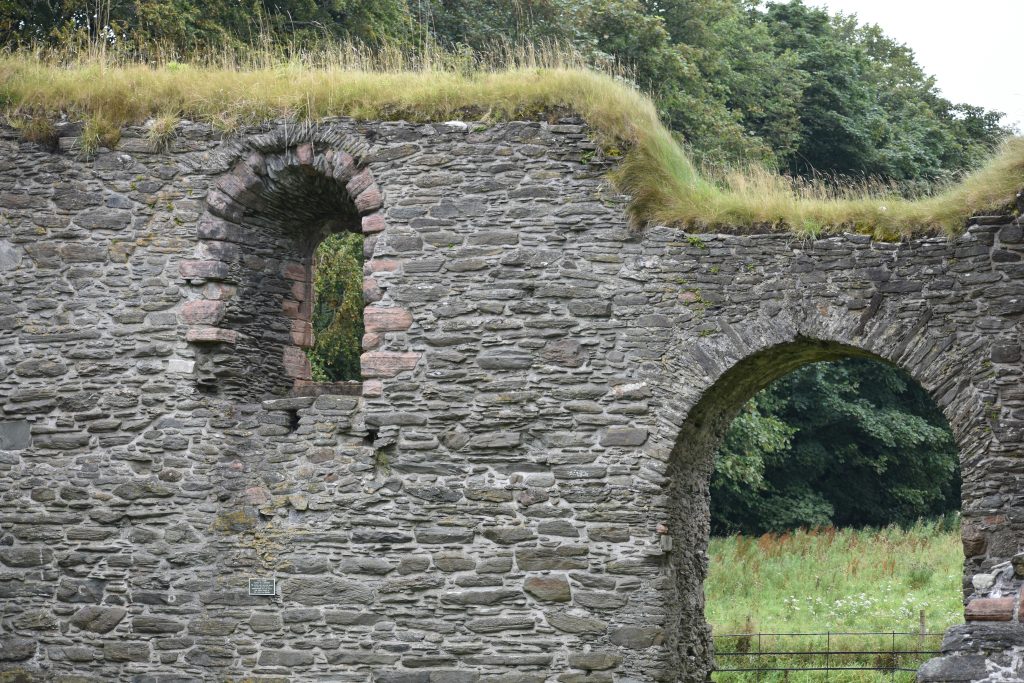 Historische Steinmauer mit Rundbögen und Grasbewuchs auf mittelalterlichen Mauerresten.